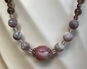 A beaded necklace in shades of purple featuring a center shell bead